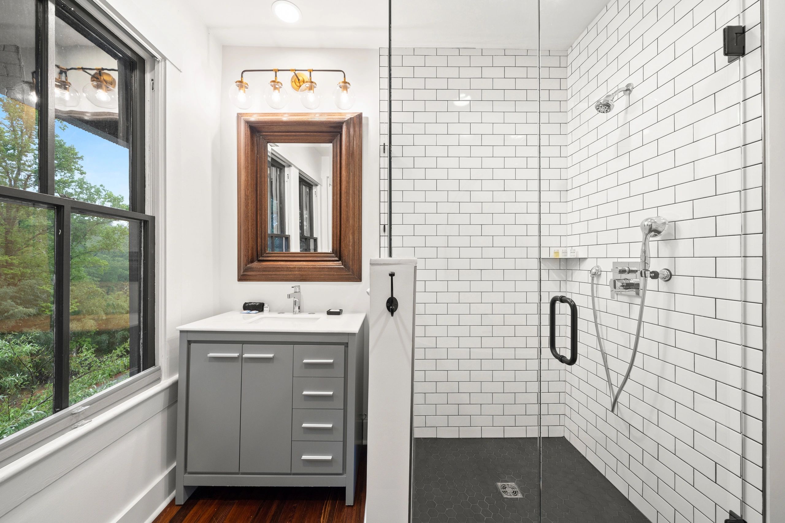 Modern bathroom with glass shower and gray vanity under a large window